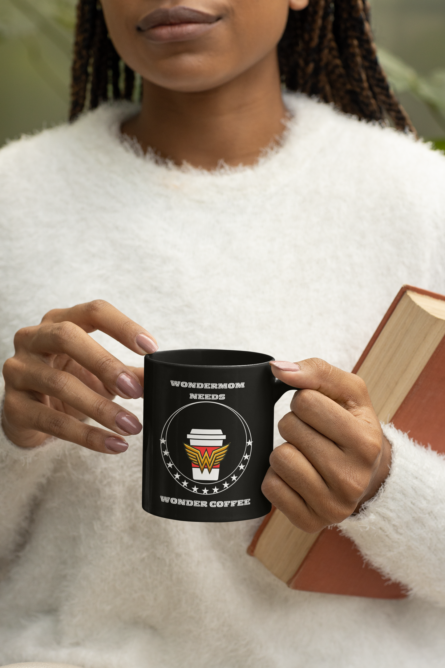 Black ceramic mug with WonderMom coffee design held by woman in cozy sweater, ideal for gifting to moms who run on caffeine and love.