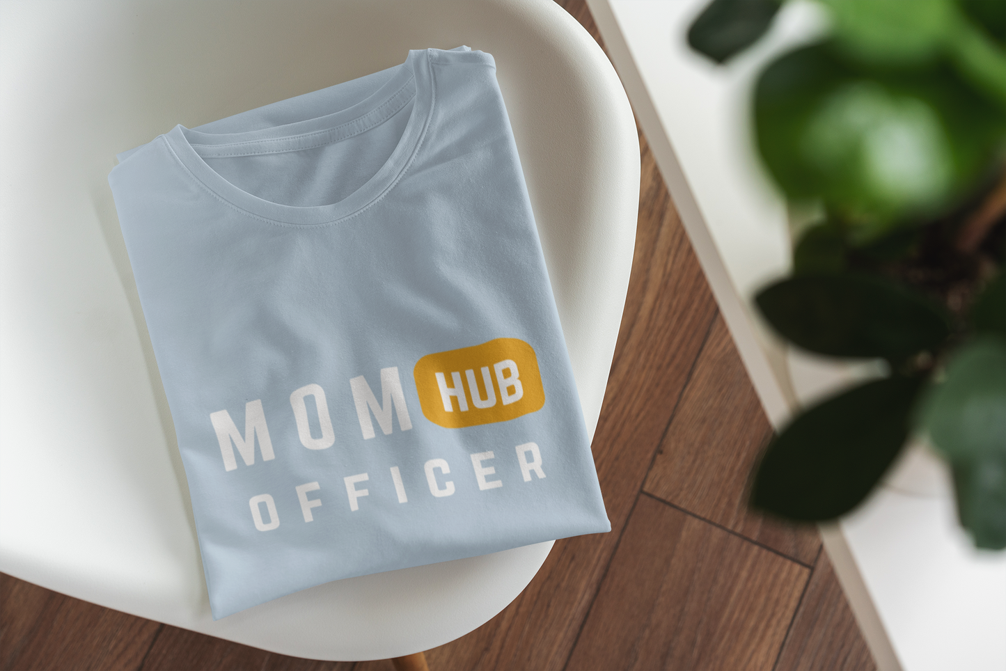 Light‑blue mom life shirt folded on modern chair, featuring bold “Mom Hub Officer” graphic for organized moms.