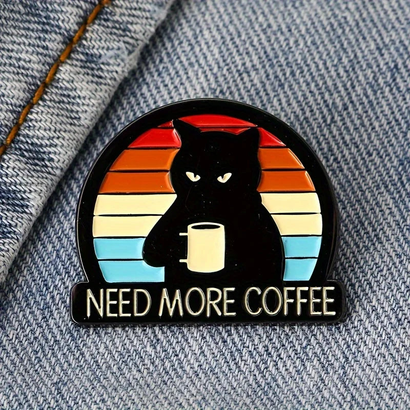 Need More Coffee cat brooch fastened to blue denim jacket, vibrant enamel accessory for pin collectors.