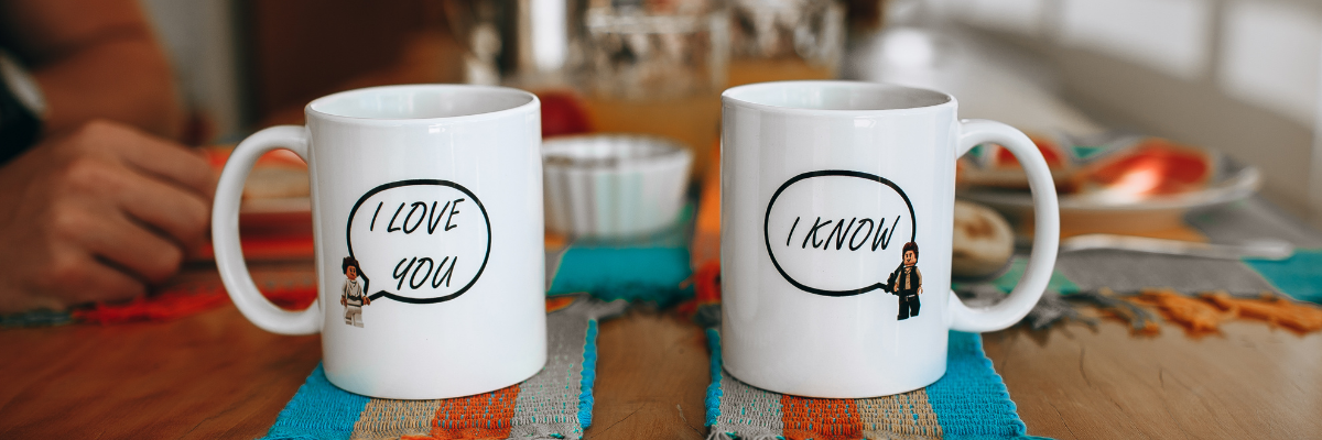 Two white ceramic mugs on a breakfast table, each with matching “I Love You / I Know” speech-bubble designs.