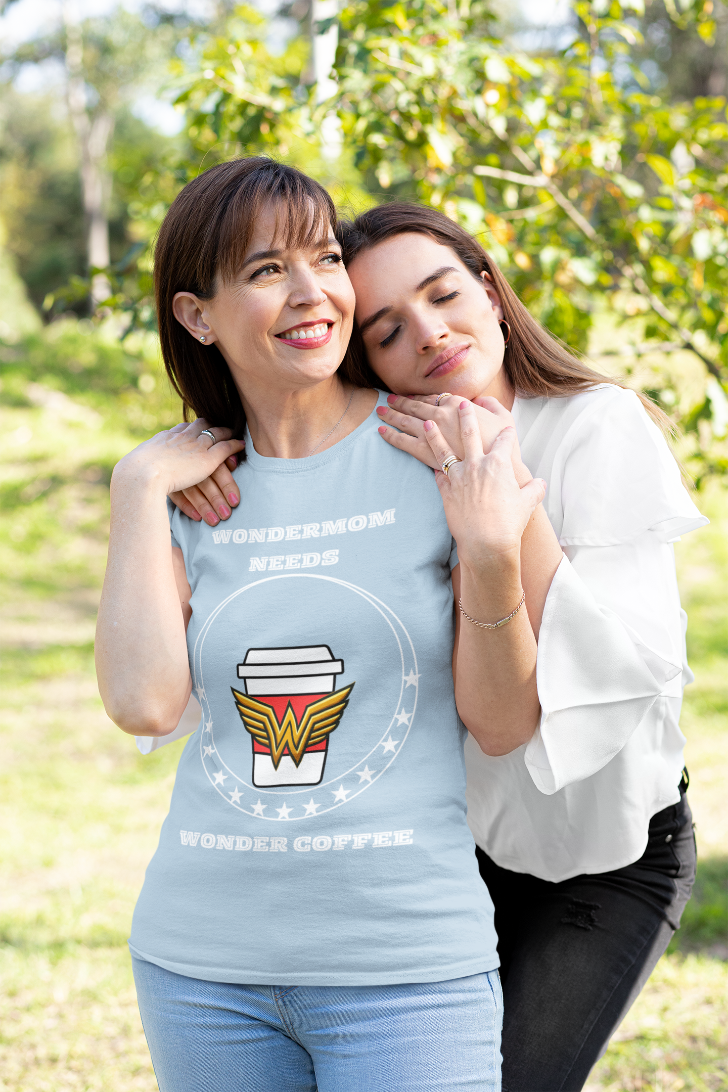 Light‑blue mom life shirt with WonderMom coffee emblem worn by mother hugging her adult daughter in sunny garden.
