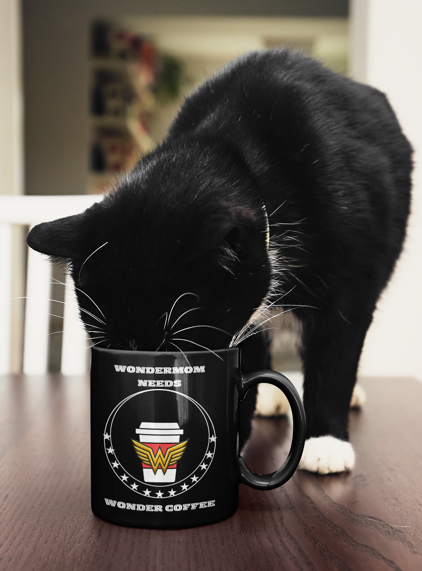 Black ceramic mug with “WonderMom Needs Wonder Coffee” design being curiously sniffed by a black-and-white cat, showing playful, homey lifestyle use.