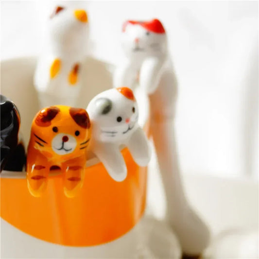 Close‑up of ceramic cat coffee spoons perched on an orange mug rim—adorable funny gifts for caffeine lovers.

