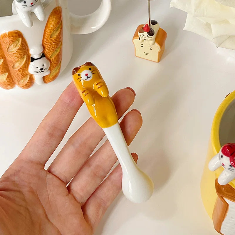 Hand holding tiger‑striped cat coffee spoon over breakfast setup—charming single‑serve funny gifts utensil.

