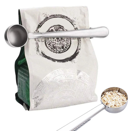 Stainless steel coffee scoop sealing a bag of ground coffee with built‑in clip.