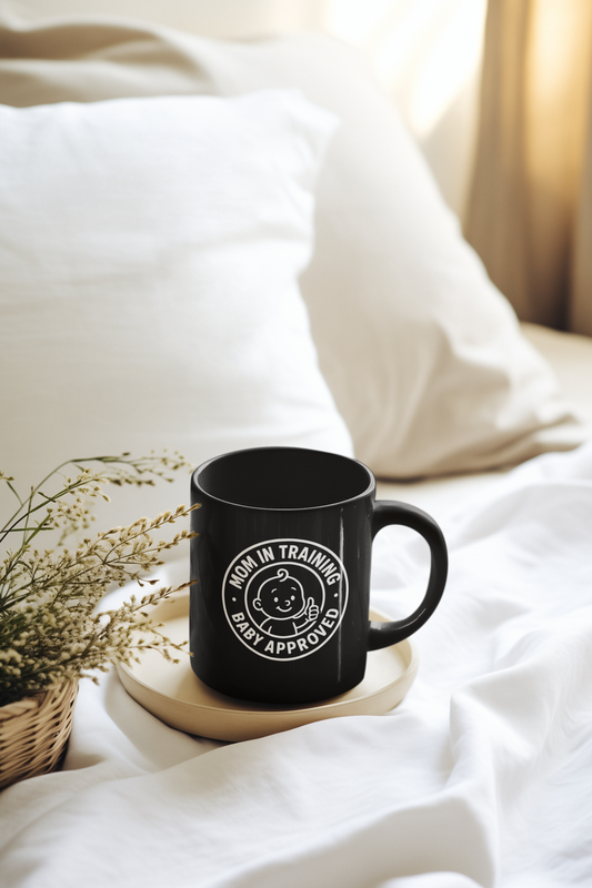 Black ceramic mug with “Mom in Training, Baby Approved” design placed on a bed tray, ideal for new moms enjoying coffee in comfort.