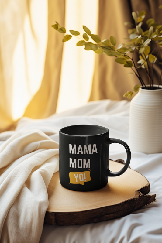 Black ceramic mug with “Mama Mom Yo!” text design placed on a cozy bed tray, ideal Mother’s Day gift for moms who juggle it all.
